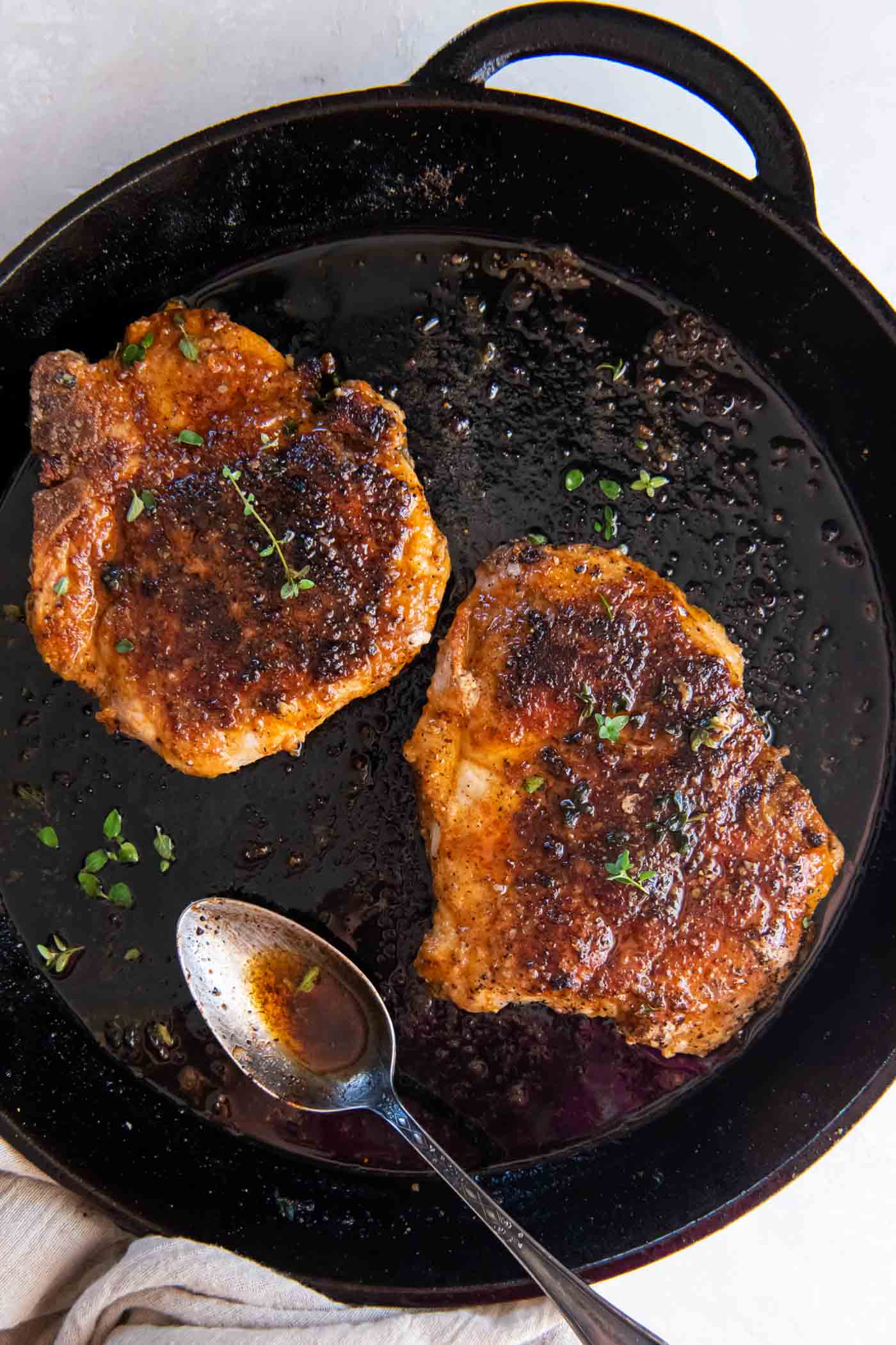 These pan fried pork chops are juicy and tender with the best flavorful browned crust. Learn how to cook pork chops in a skillet using bone in or boneless pork chops. This is one of the best easy pork chop recipes! Two pan fried pork chops in a cast iron skillet with a spoon.